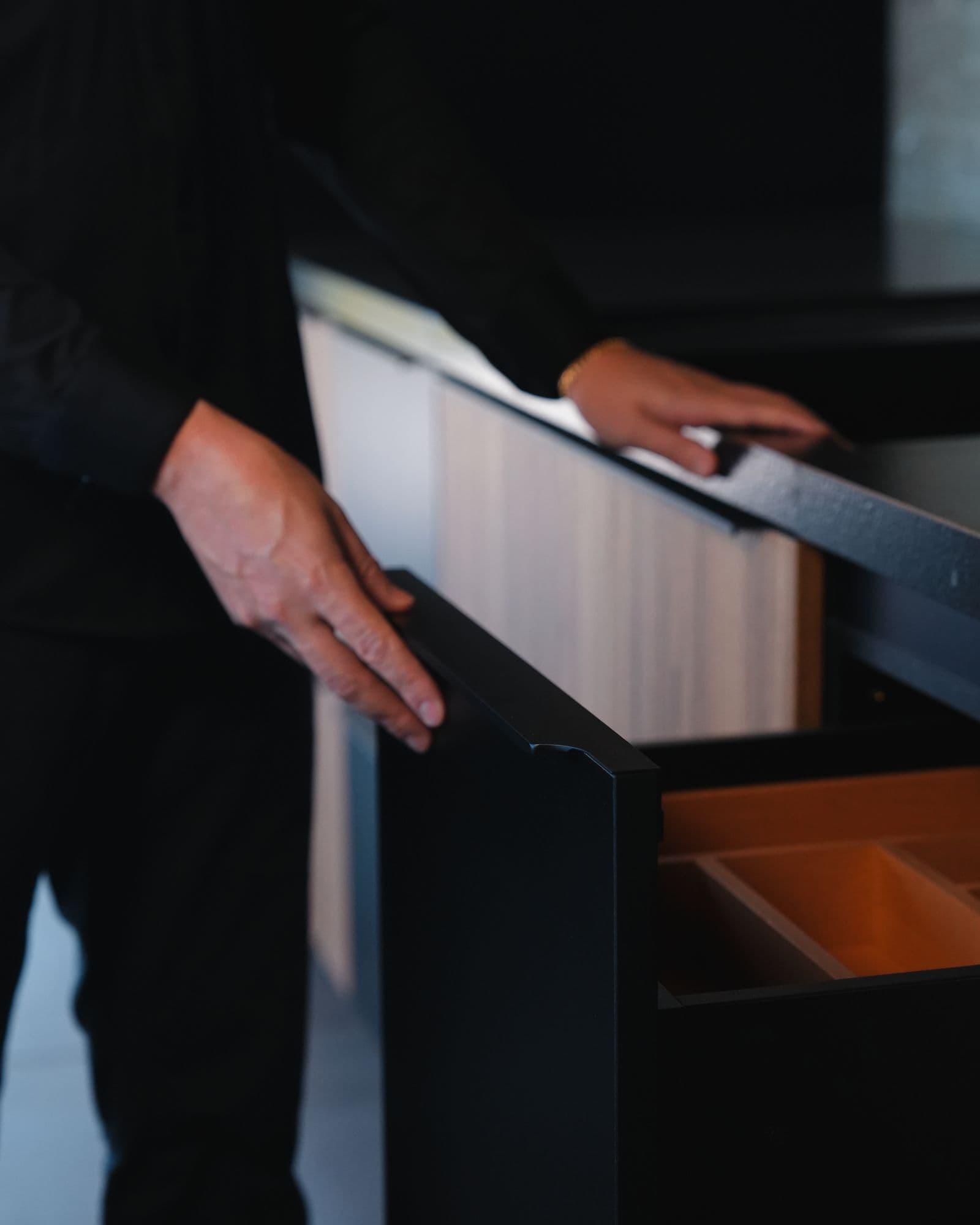 Mão fechando uma gaveta com interior de madeira em um armário preto